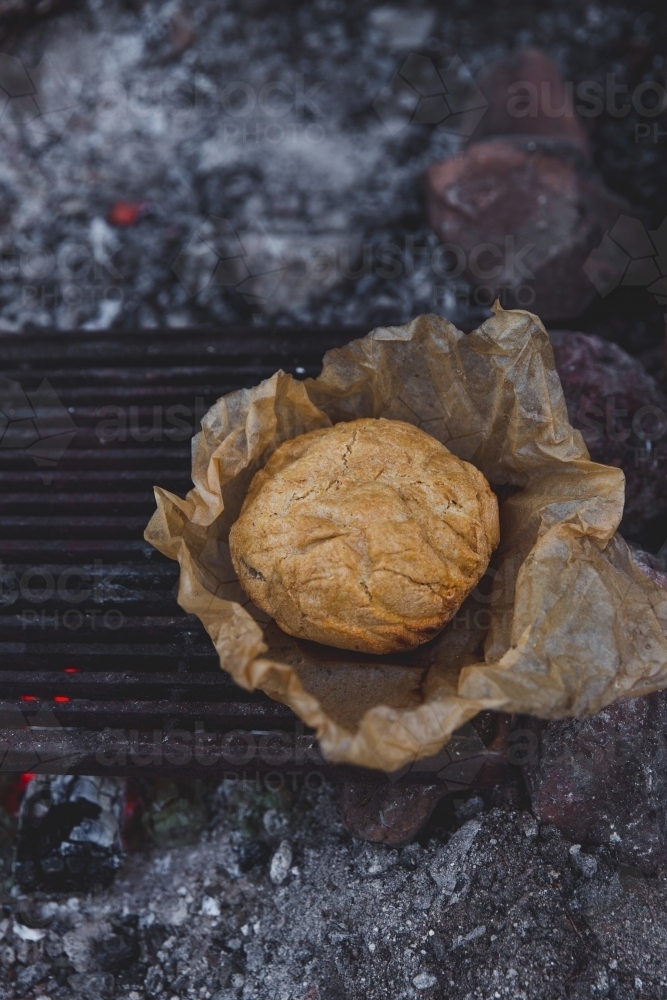 Top view of damper bread in brown baking paper on the red hot coals of a campfire - Australian Stock Image