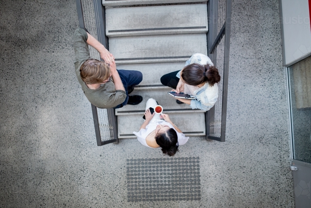 Top view of three small business workers standing on concrete stairs in an industrial office - Australian Stock Image