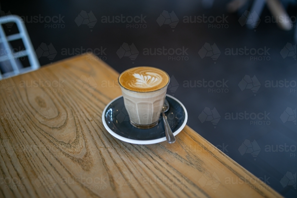 Top view shot of a coffee with an art in a cup with a cup coaster and a teaspoon on a table - Australian Stock Image