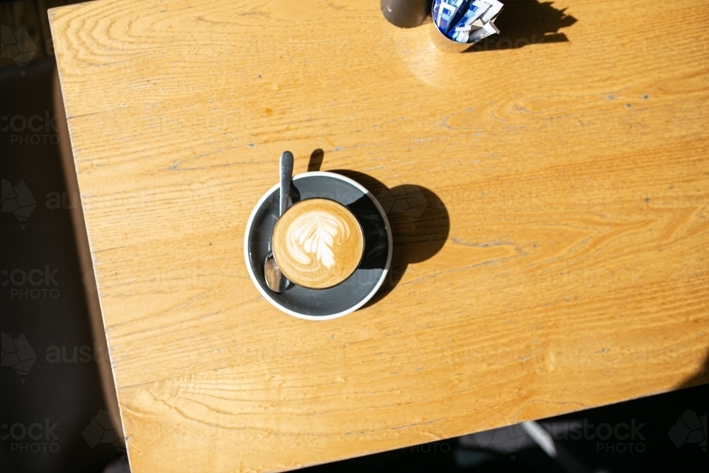 Top view shot of a coffee with an art in a small mug with a cup coaster and a teaspoon on a table - Australian Stock Image