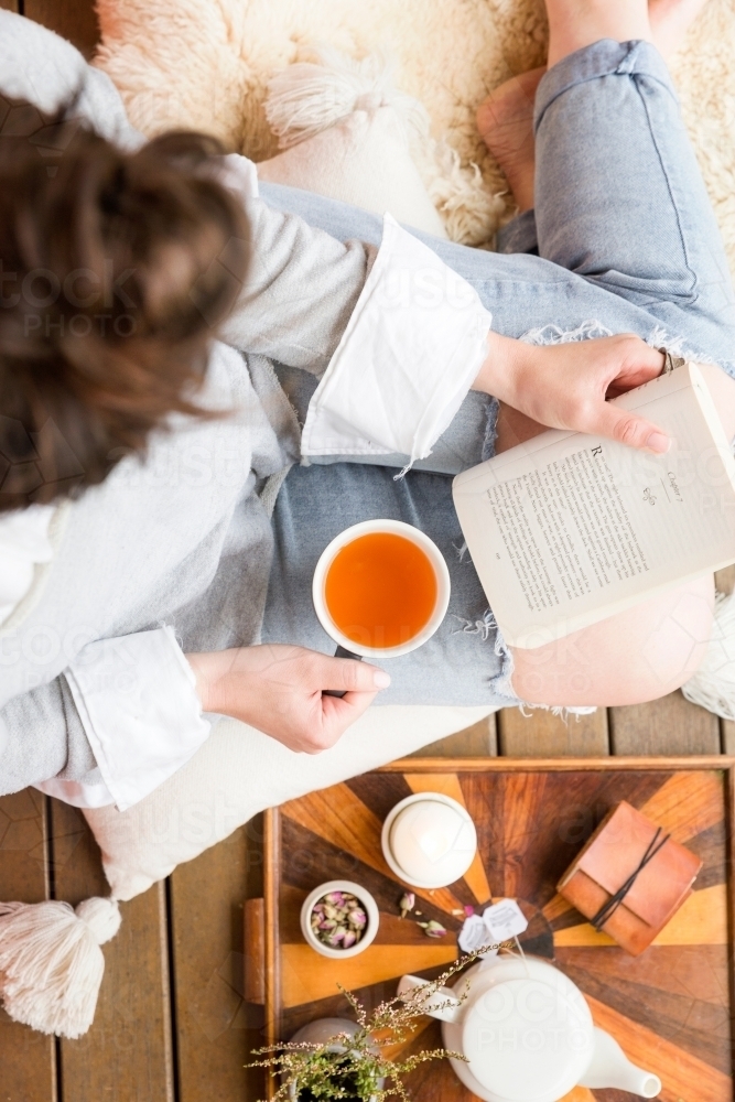 Top view shot of a woman reading a book and drinking tea - Australian Stock Image