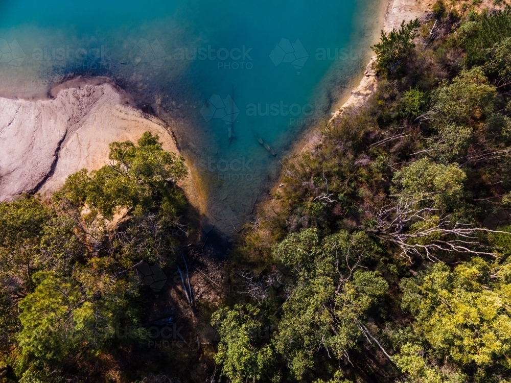 top view shot of blue lake water with bush hills and green trees and white rock formation - Australian Stock Image