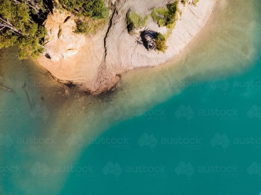 top view shot of blue lake water with green trees and white rock formation - Australian Stock Image