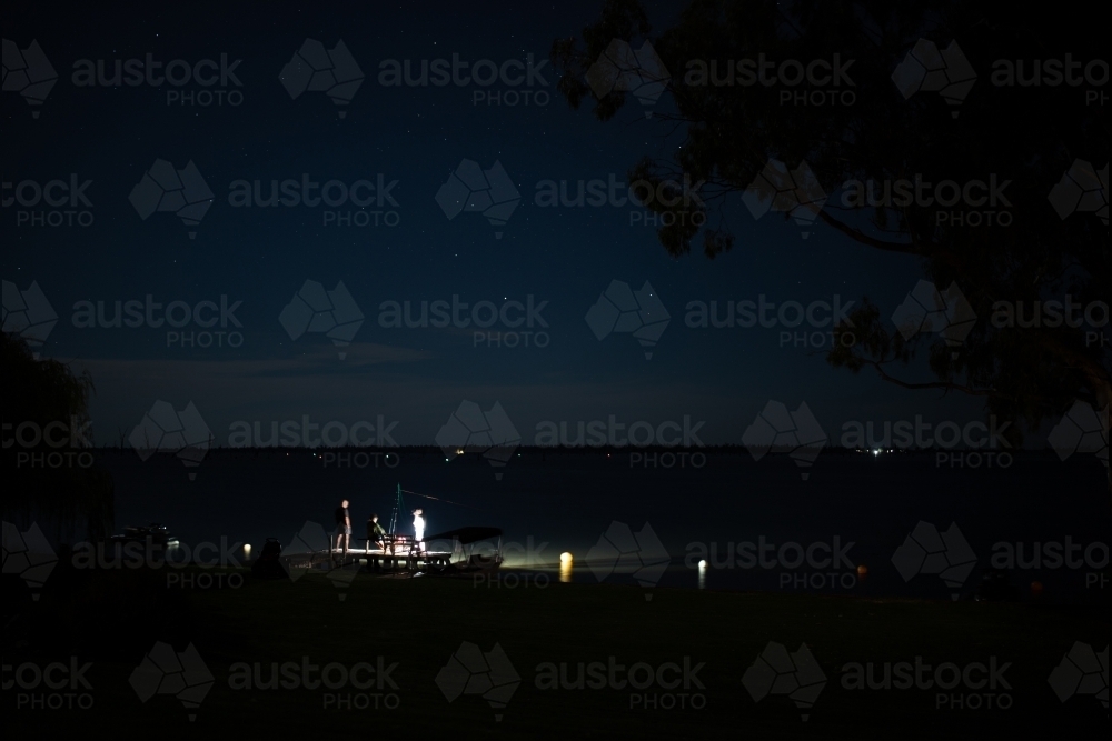 Torch lit people fishing on lake jetty at night - Australian Stock Image