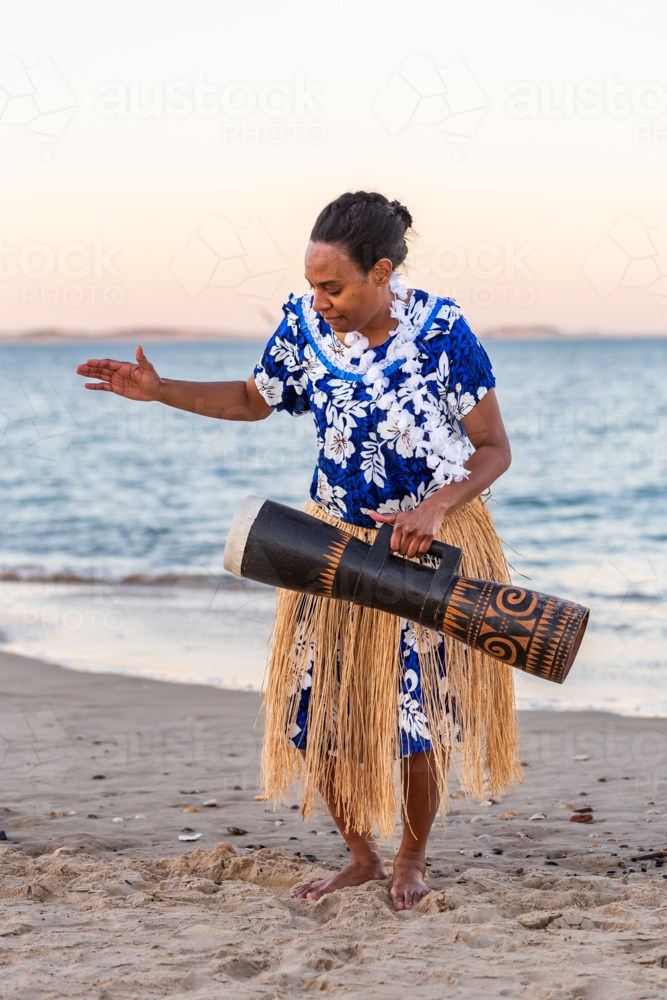 Torres Strait Island dance performer in traditional floral dress holding drum by ocean - Australian Stock Image
