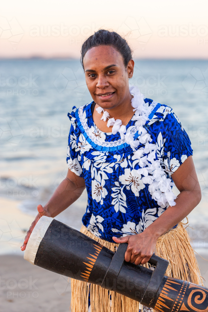 Torres Strait Island dance performer in traditional floral dress holding drum by ocean - Australian Stock Image