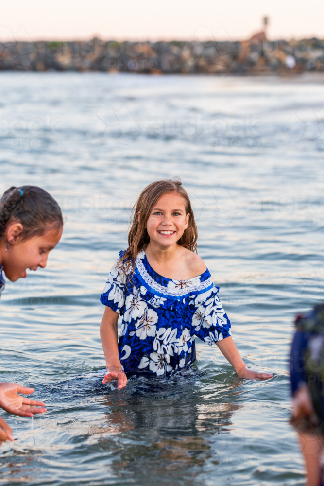 Torres Strait Islander child wading in ocean water at dusk wearing traditional floral dress - Australian Stock Image