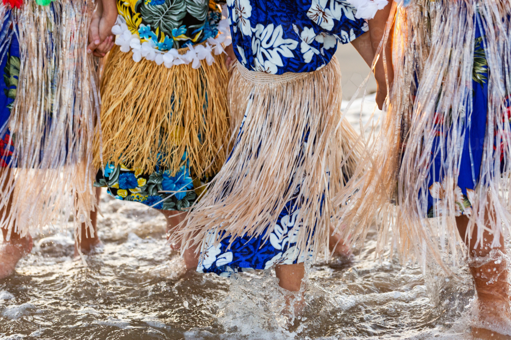 Torres Strait Islander children in traditional floral dresses and skirts standing together in ocean - Australian Stock Image