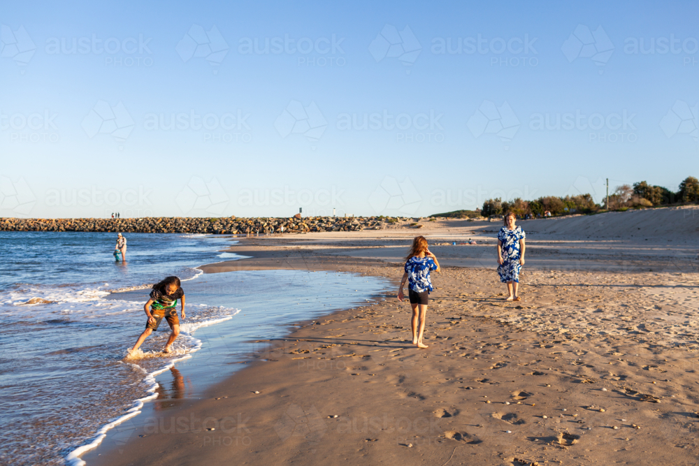 Torres Strait Islander children playing together at beach boy running from waves - Australian Stock Image