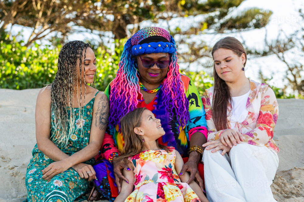 Torres Strait Islander family with grandmother mum and daughters sitting on sand dune at the beach - Australian Stock Image