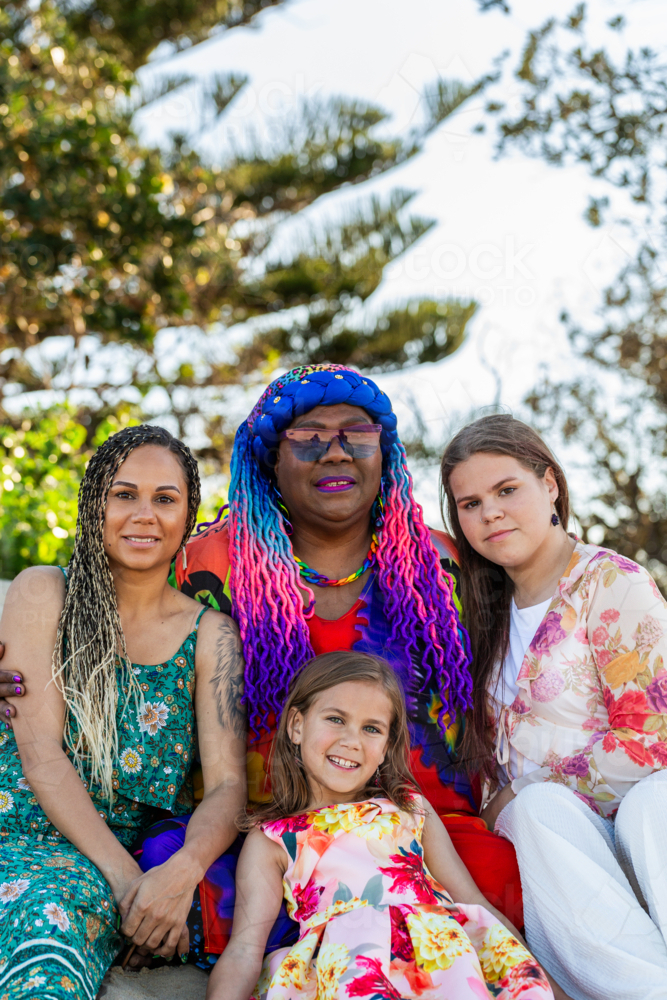 Torres Strait Islander family with grandmother mum and daughters sitting on sand dune at the beach - Australian Stock Image
