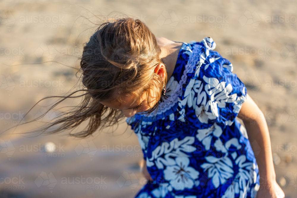 Torres Strait Islander girl at beach on windy day wearing traditional floral dress - Australian Stock Image
