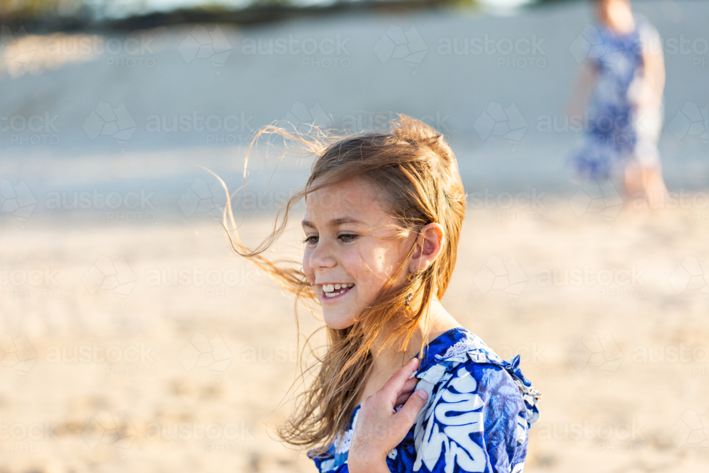 Torres Strait Islander girl at beach on windy day wearing traditional floral dress - Australian Stock Image