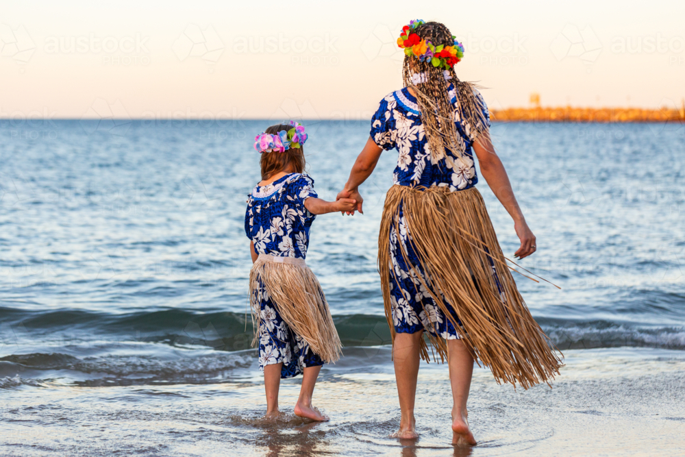Torres Strait Islander mother and young daughter in traditional floral costume and skirt by ocean - Australian Stock Image