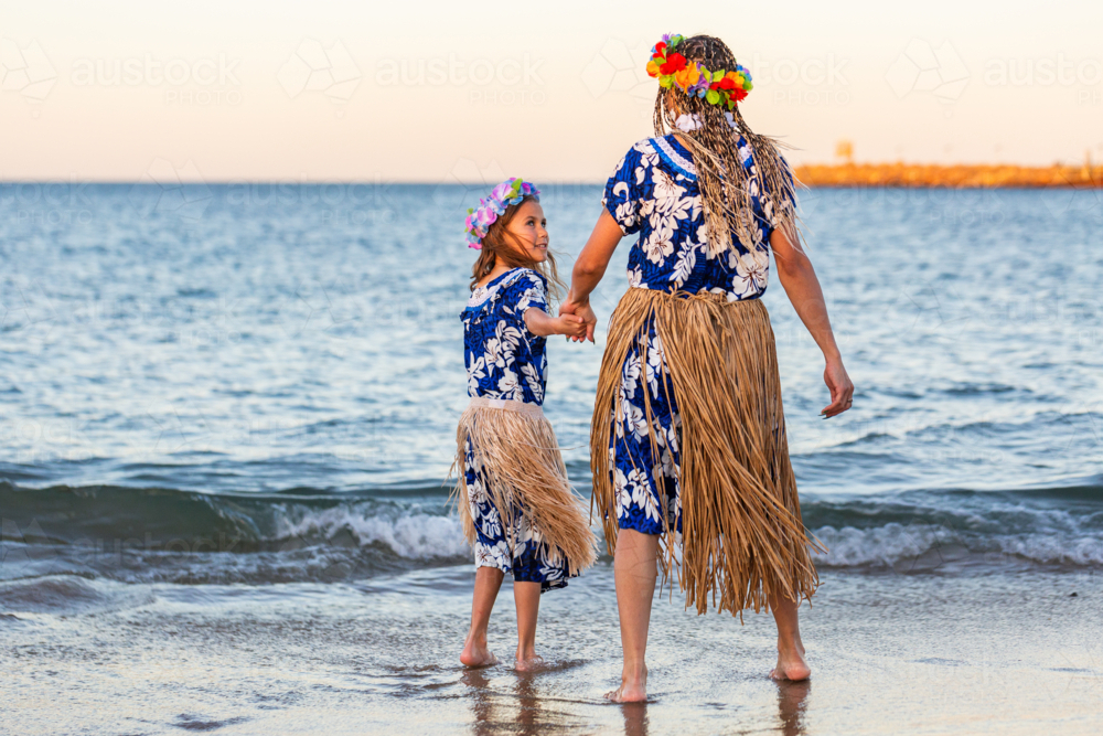 Torres Strait Islander mother and young daughter in traditional floral costume and skirt by ocean - Australian Stock Image