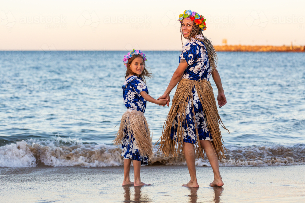 Torres Strait Islander mother and young daughter in traditional floral costume and skirt by ocean - Australian Stock Image