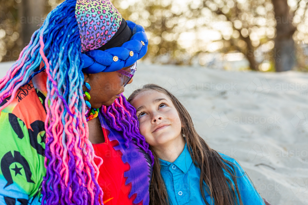 Torres Strait Islander nine year old boy with long hair sitting beside grandmother on beach - Australian Stock Image