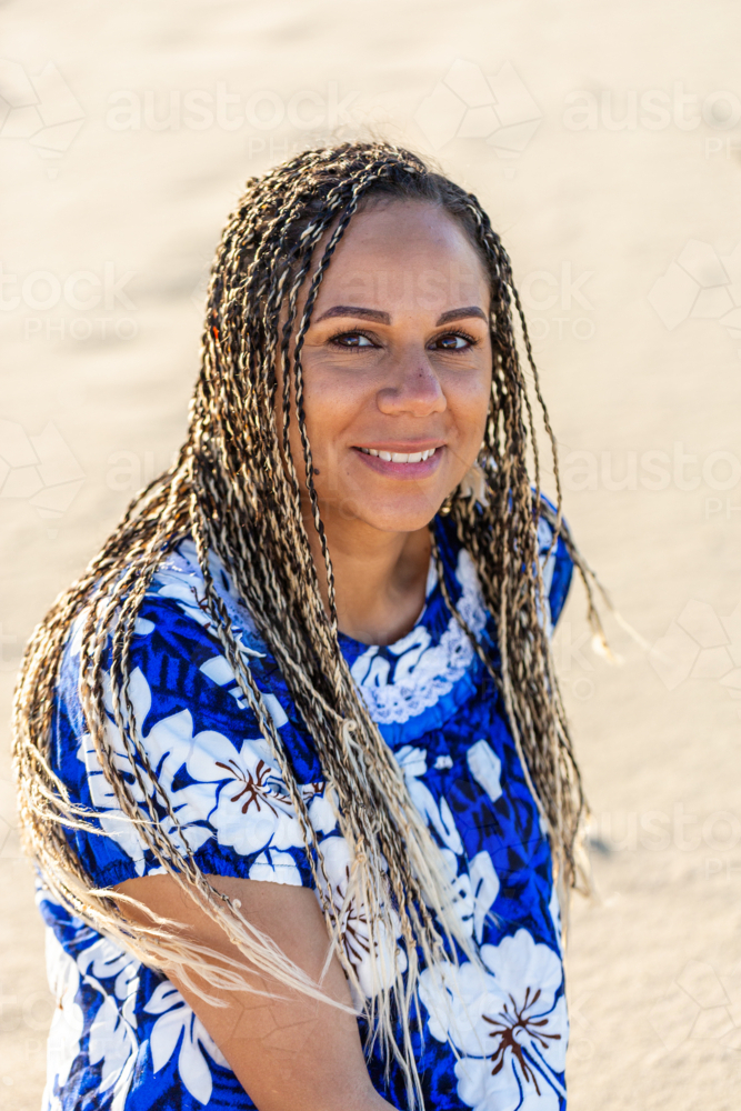 Torres Strait Islander woman in her thirties sitting in the sand on Sunny Australian beach - Australian Stock Image