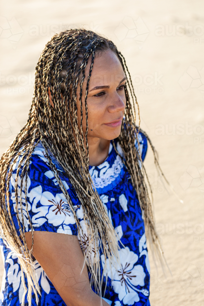 Torres Strait Islander woman in her thirties sitting in the sand on Sunny Australian beach - Australian Stock Image