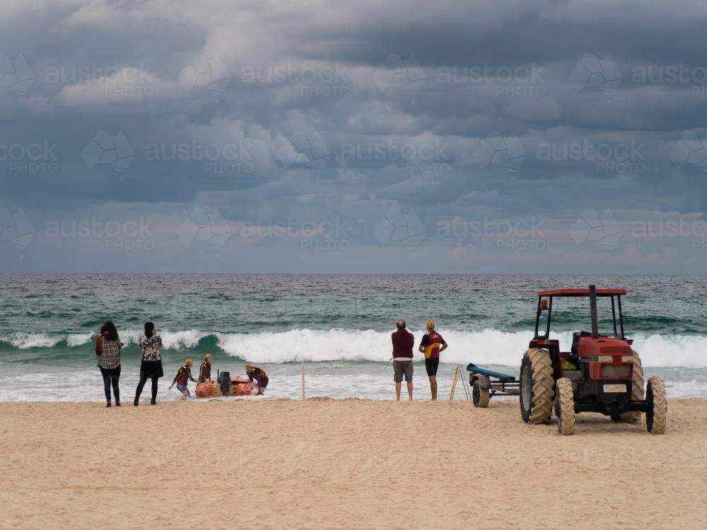 Tractor and trailer launching a boat into the surf while people watch - Australian Stock Image