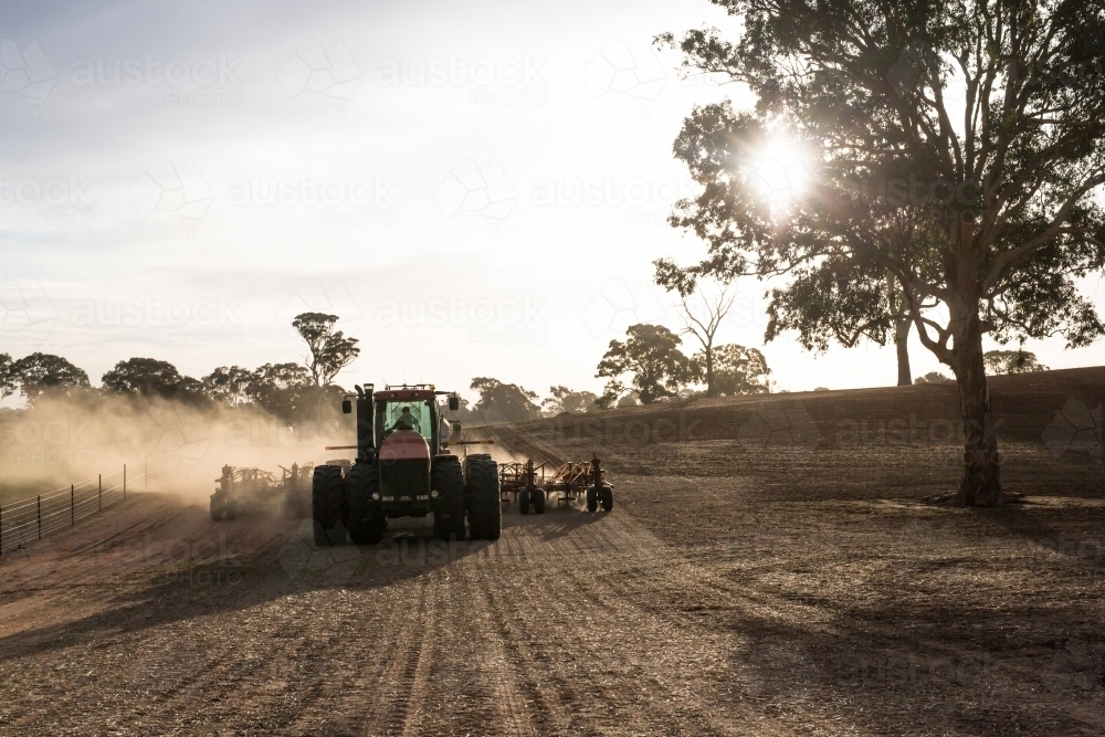 Tractor cultivating the field on a sunny day plough making dust - Australian Stock Image