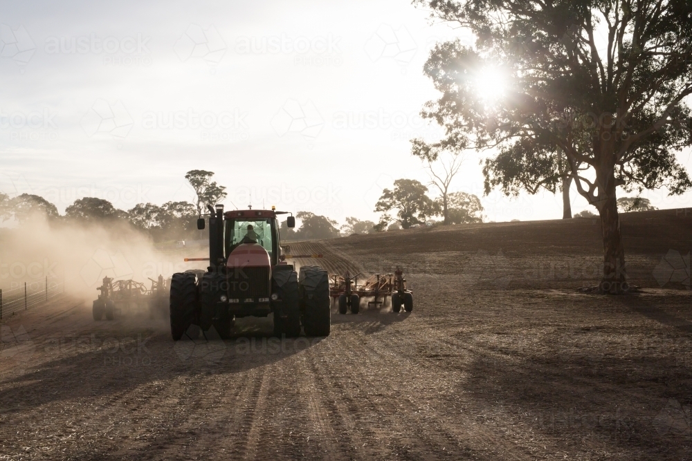 Tractor cultivating the field on a sunny day plough making dust - Australian Stock Image