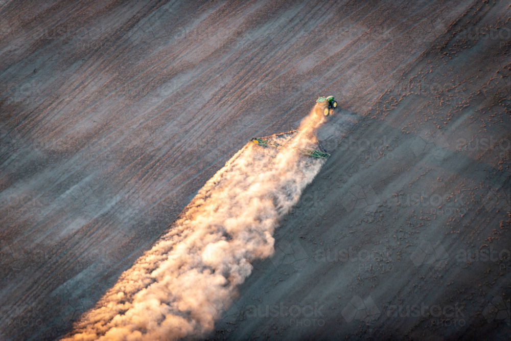 Tractor trailing dust across a dry paddock in early morning light, viewed from above - Australian Stock Image