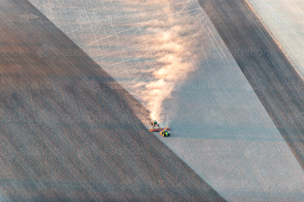 Tractor trailing dust across a dry paddock in early morning light, viewed from above - Australian Stock Image