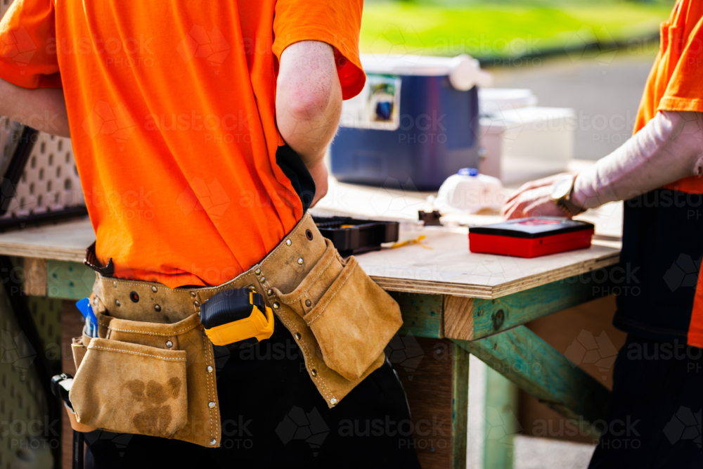 Image of trade apprentice wearing tool belt working at wooden bench ...