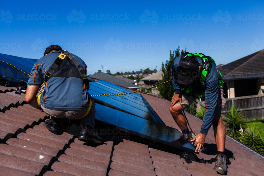 Tradesman electrician and apprentice installing solar panel system on rooftop in Australia - Australian Stock Image
