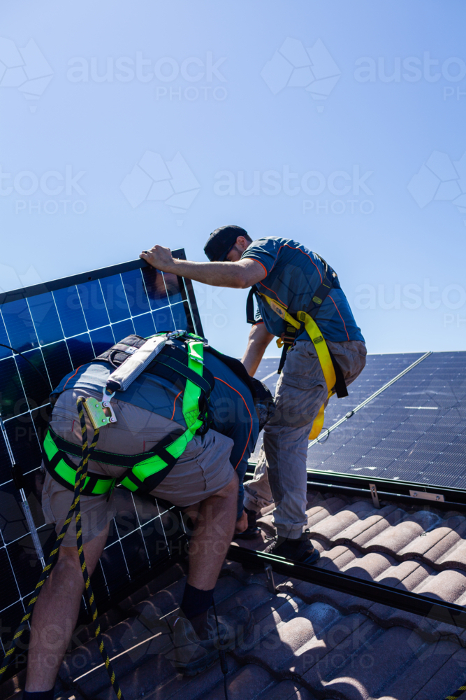 Tradesman electrician and apprentice installing solar panel system on rooftop in Australia - Australian Stock Image