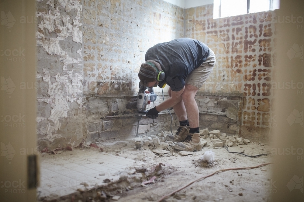 Tradesman jackhammering a floor in a home renovation - Australian Stock Image