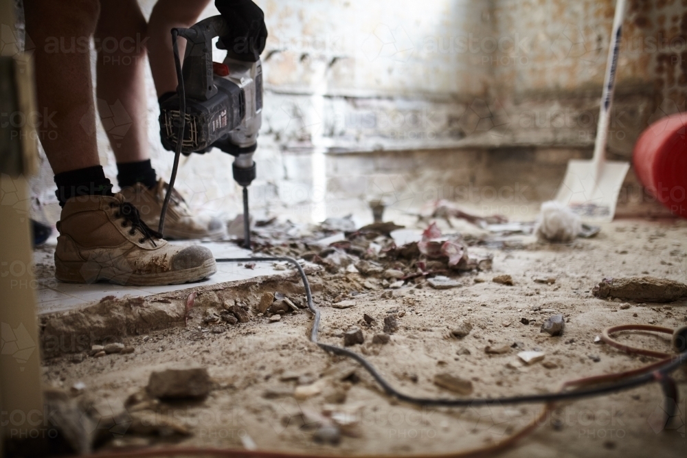 Tradesman jackhammering bathroom tiles in a home renovation - Australian Stock Image