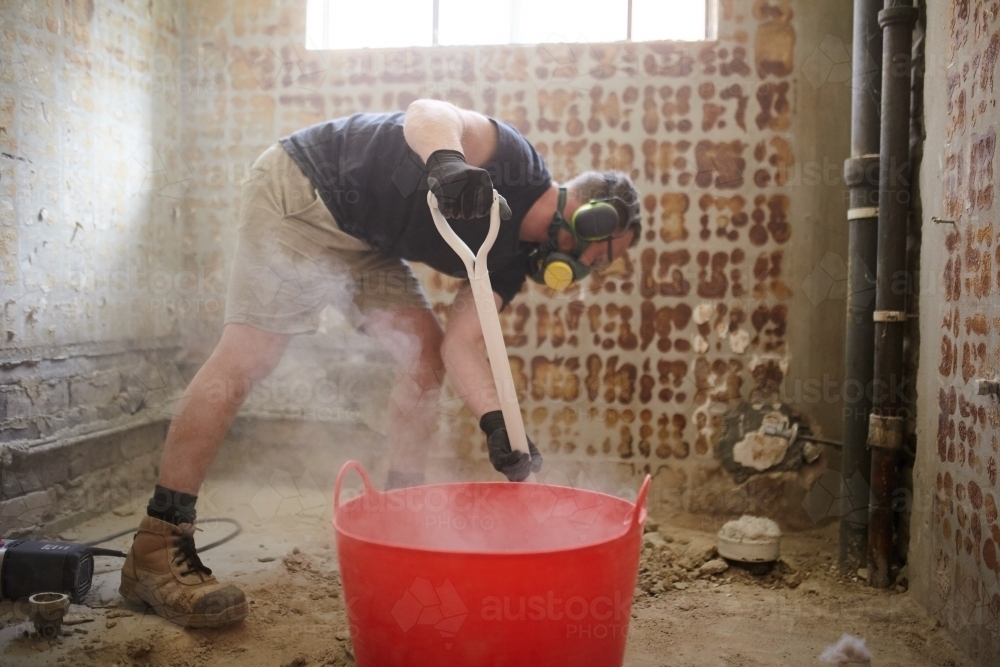 Tradesman shovelling debris into a bucket in a construction zone - Australian Stock Image