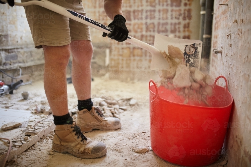 Tradesman shovelling debris into a bucket in a construction zone - Australian Stock Image