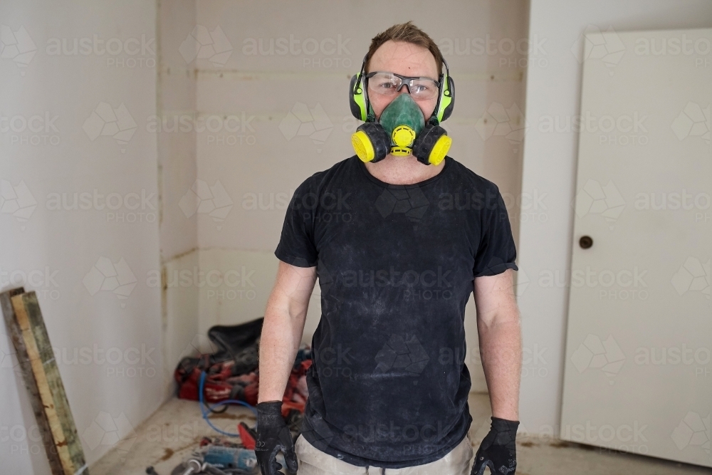 Tradesman standing in a room in a construction zone wearing protective equipment - Australian Stock Image