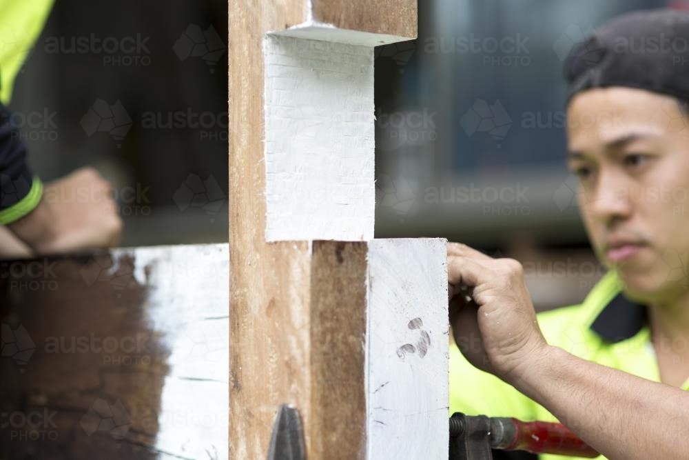 Tradesmen adjusting a wooden beam for a deck on a home renovation site. - Australian Stock Image