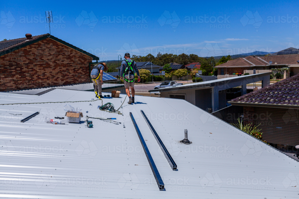 Tradesmen in safety harness equipment installing rails for solar panel system on Australian roof - Australian Stock Image
