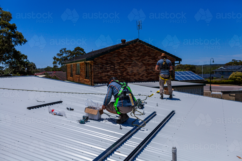 Tradesmen in safety harness equipment installing rails for solar panel system on Australian roof - Australian Stock Image