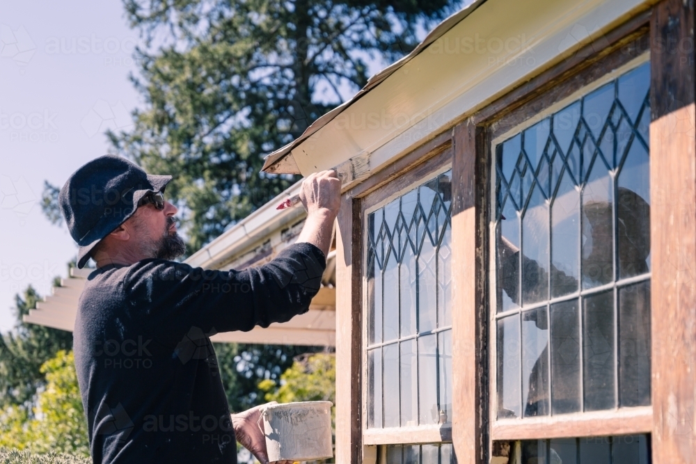 Tradesperson painting exterior windows of country home - Australian Stock Image