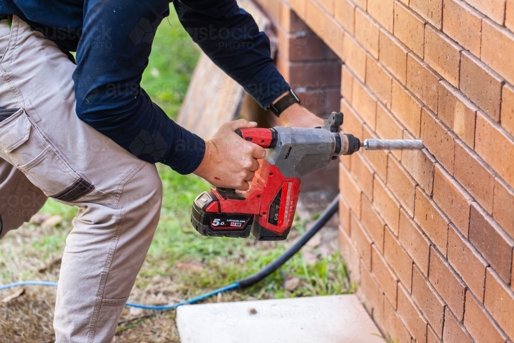 Image of Tradie drilling hole in wall of house Austockphoto