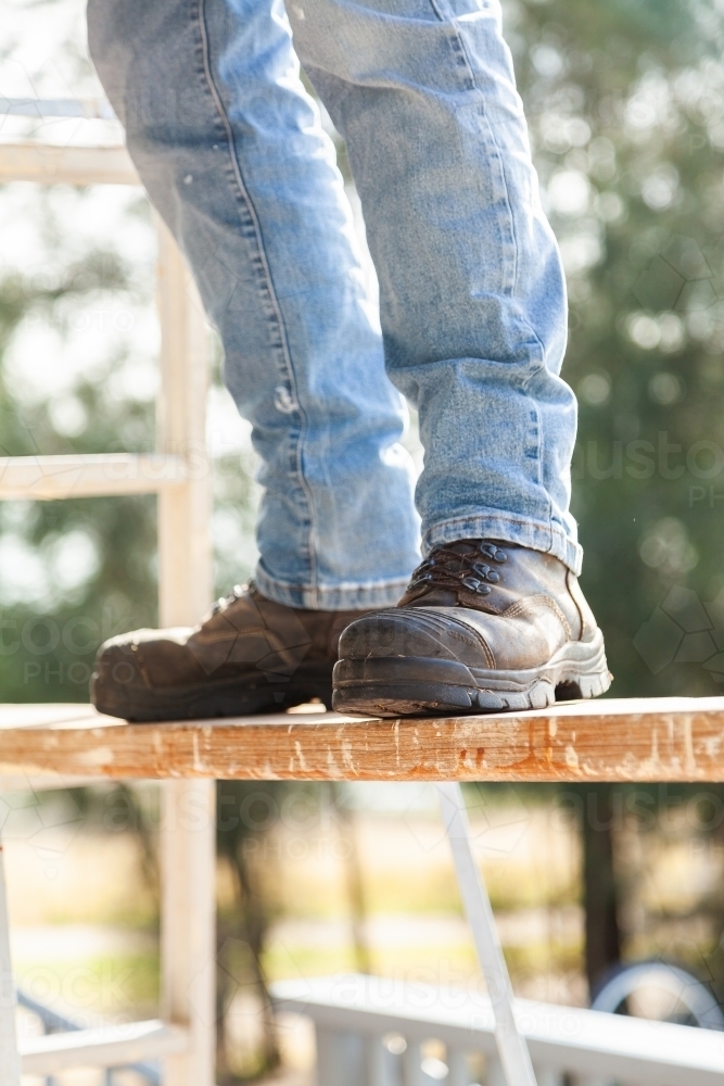 Tradie feet and boots on plank for painting high up - Australian Stock Image