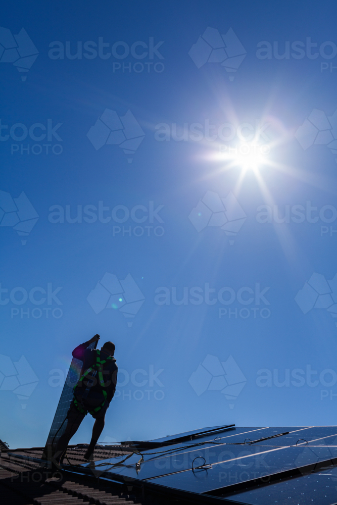 Image of Tradie man laying solar panel on roof under blue sky and sun ...