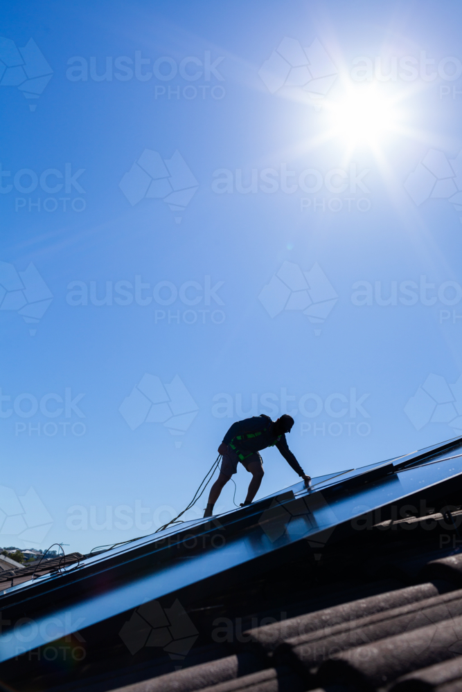 Image of Tradie man laying solar panel on roof under blue sky during ...
