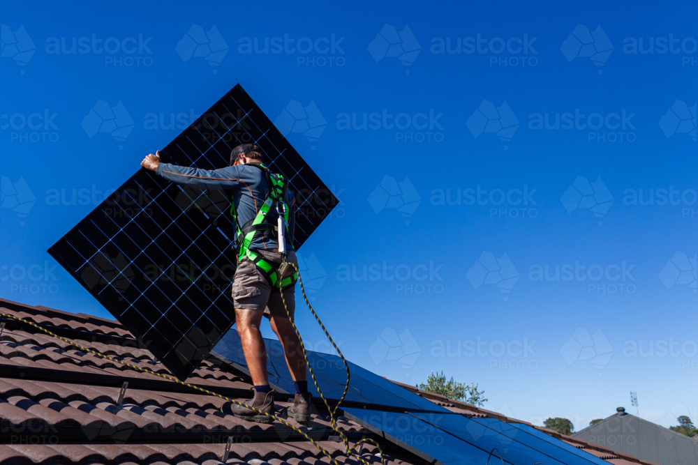 Image of Tradie man laying solar panel on roof under blue sky during ...
