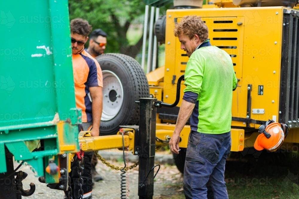 Tradies securing wood chipper machine onto truck - Australian Stock Image