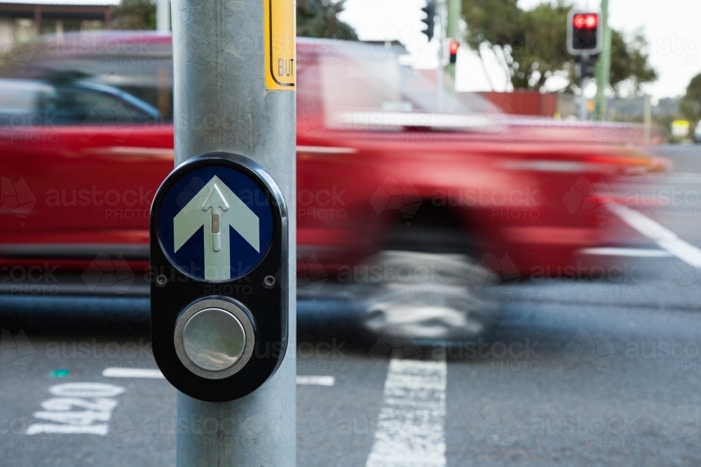 Traffic pedestrian crossing light button with cars zooming past - Australian Stock Image
