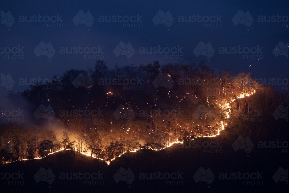 Trail of fire coming over a ridge during dusk - Australian Stock Image