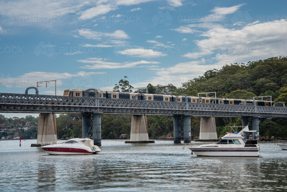 Train going over the rail bridge at Como in Sydney with moored boats in the foreground. - Australian Stock Image