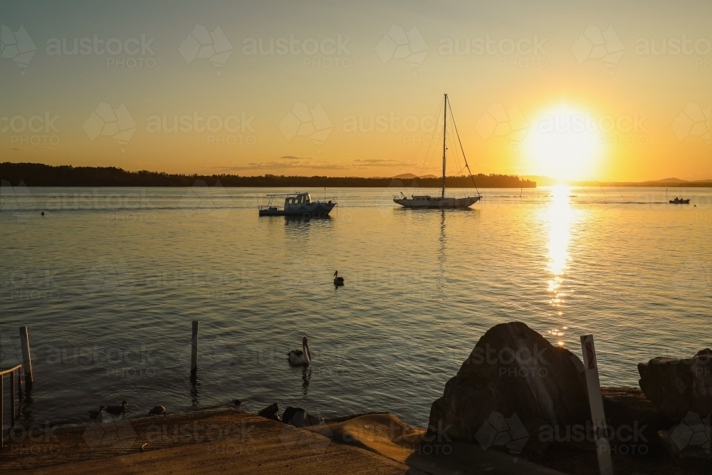 Tranquil afternoon setting with silhouette of pelicans and yachts on the river at sunset - Australian Stock Image